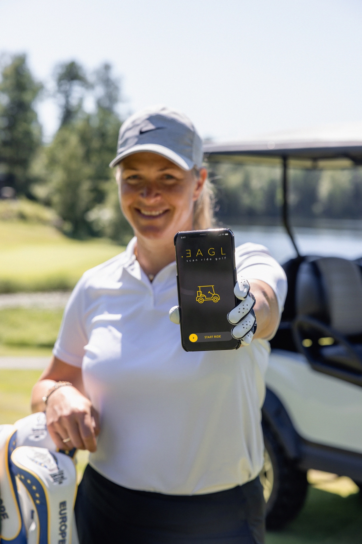 Golfer holding up the EAGL app on a smartphone beside a golf cart